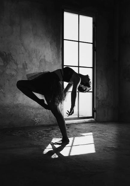 Graceful ballerina dancing in house with shadow on floor