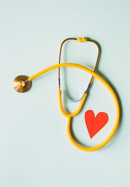 Medical stethoscope with red paper heart on white surface