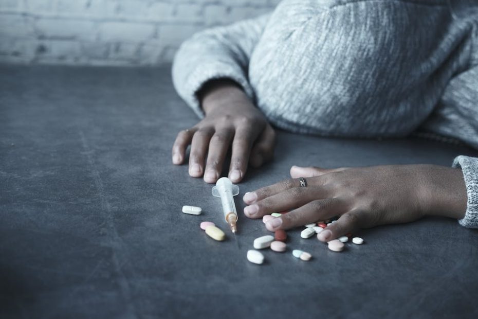 Close-up Photo of Person lying beside a Syringe and Tablets