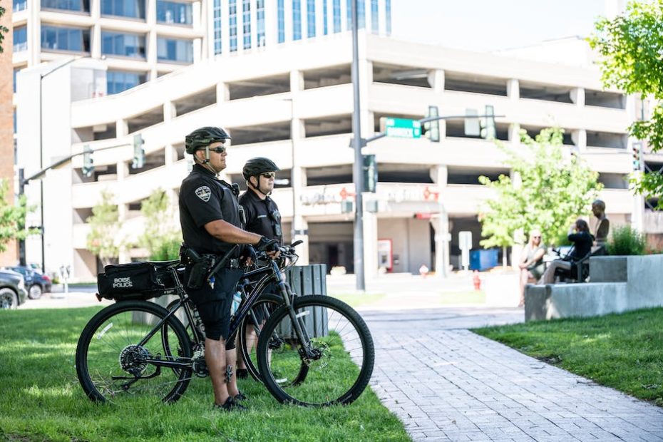 Side view full length serious bicycle patrol policemen in uniforms and helmets standing on city lawn