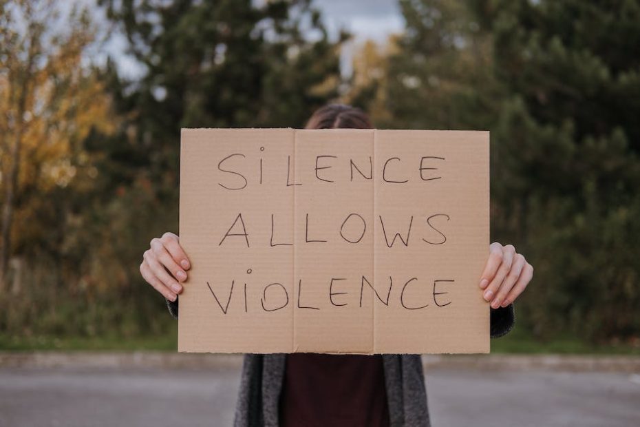 Anonymous person showing slogan silence allows violence on cardboard on road near green trees