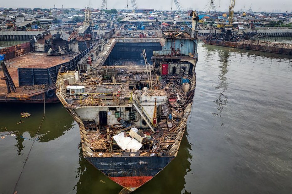 From above of aged rusty ship with rubbish moored in abandoned port in cloudy day in daylight