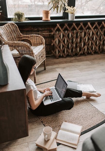 Young barefoot woman using laptop on floor near books in stylish living room